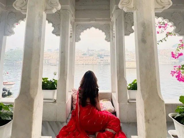 A woman in a red dress sitting in a white marble pavilion overlooking a lake.