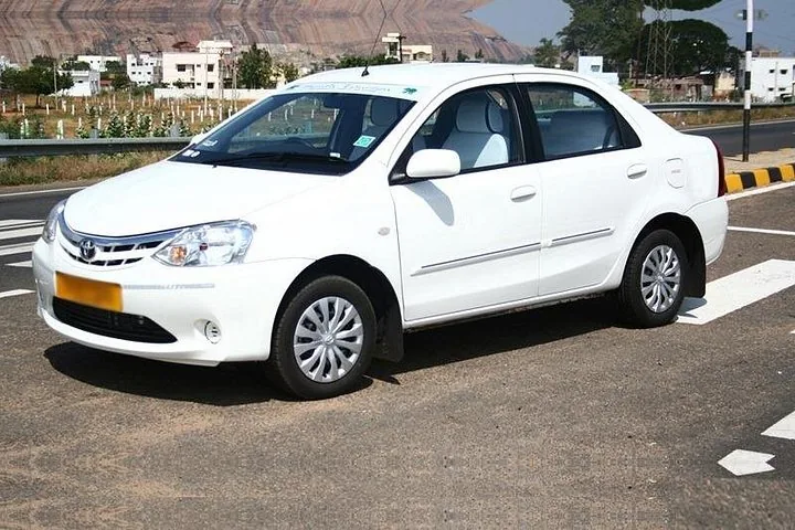 A white Toyota Etios car parked on a road with hills in the background.