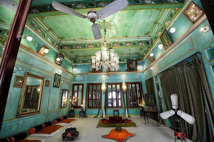 An interior room with turquoise walls, a patterned ceiling, and a large chandelier.