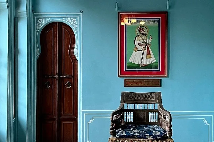 A framed portrait of a historical figure on a blue wall above an ornate chair.