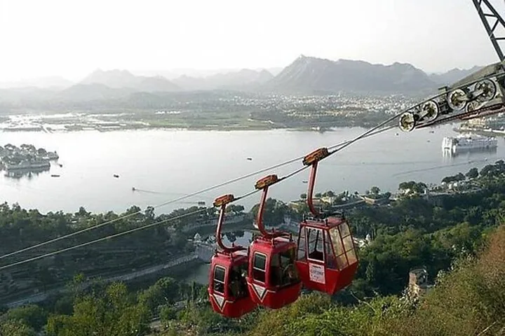 Red cable cars of Mansapurna Karni Mata Ropeway with a scenic view of a lake.